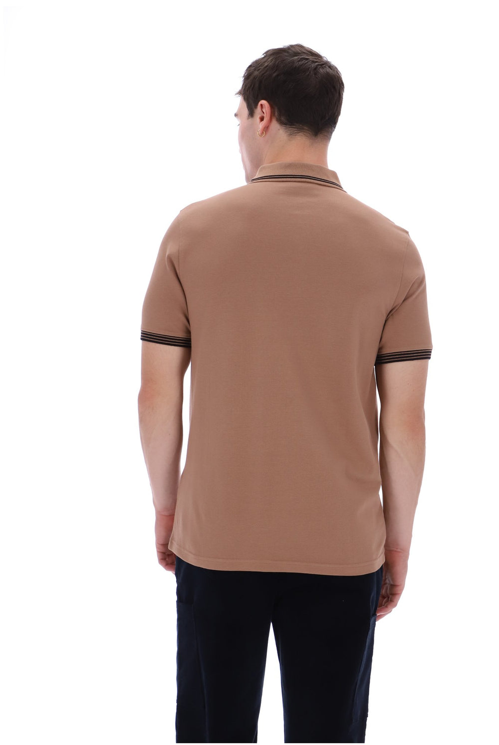 A man viewed from the back wearing a tan short-sleeve polo shirt with dark trim on the collar and sleeve cuffs, paired with dark trousers, against a plain white background.