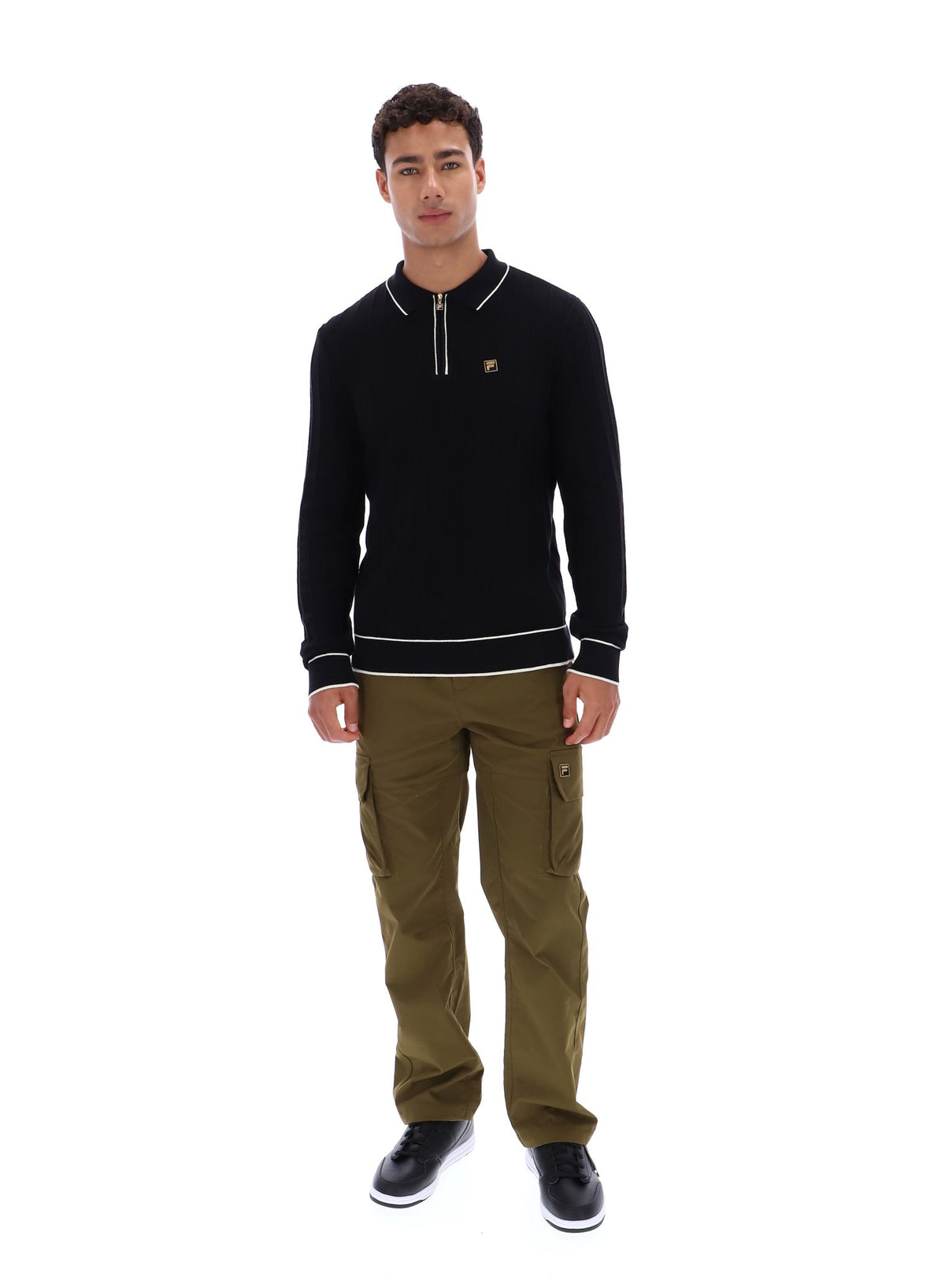 Man wearing a black sweater with white trim and a small FILA Gold logo on the chest, paired with green FILA cargo pants, against a white background