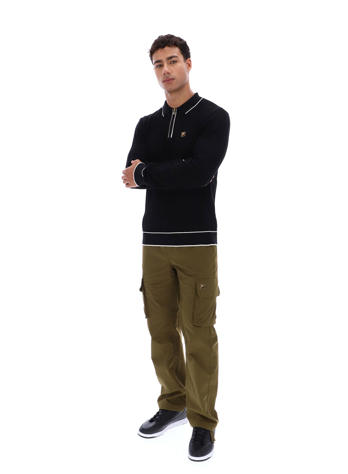Man wearing a black sweater with white trim and a small FILA Gold logo on the chest, paired with green FILA cargo pants, against a white background