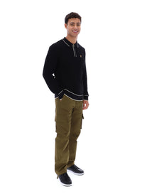 Man wearing a black sweater with white trim and a small FILA Gold logo on the chest, paired with green FILA cargo pants, against a white background