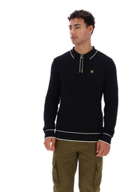 Man wearing a black sweater with white trim and a small FILA Gold logo on the chest, paired with green FILA cargo pants, against a white background