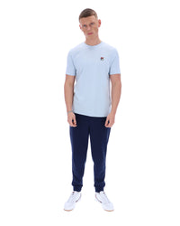 Man wearing a light blue t-shirt and navy tracksuit pants on a white background