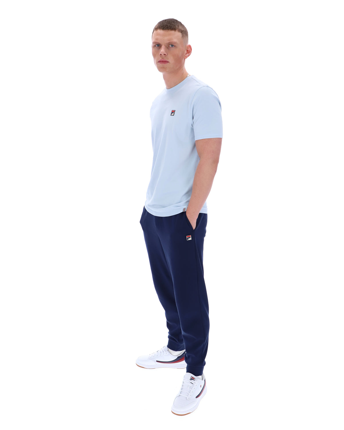 Man wearing a light blue t-shirt and navy tracksuit pants on a white background