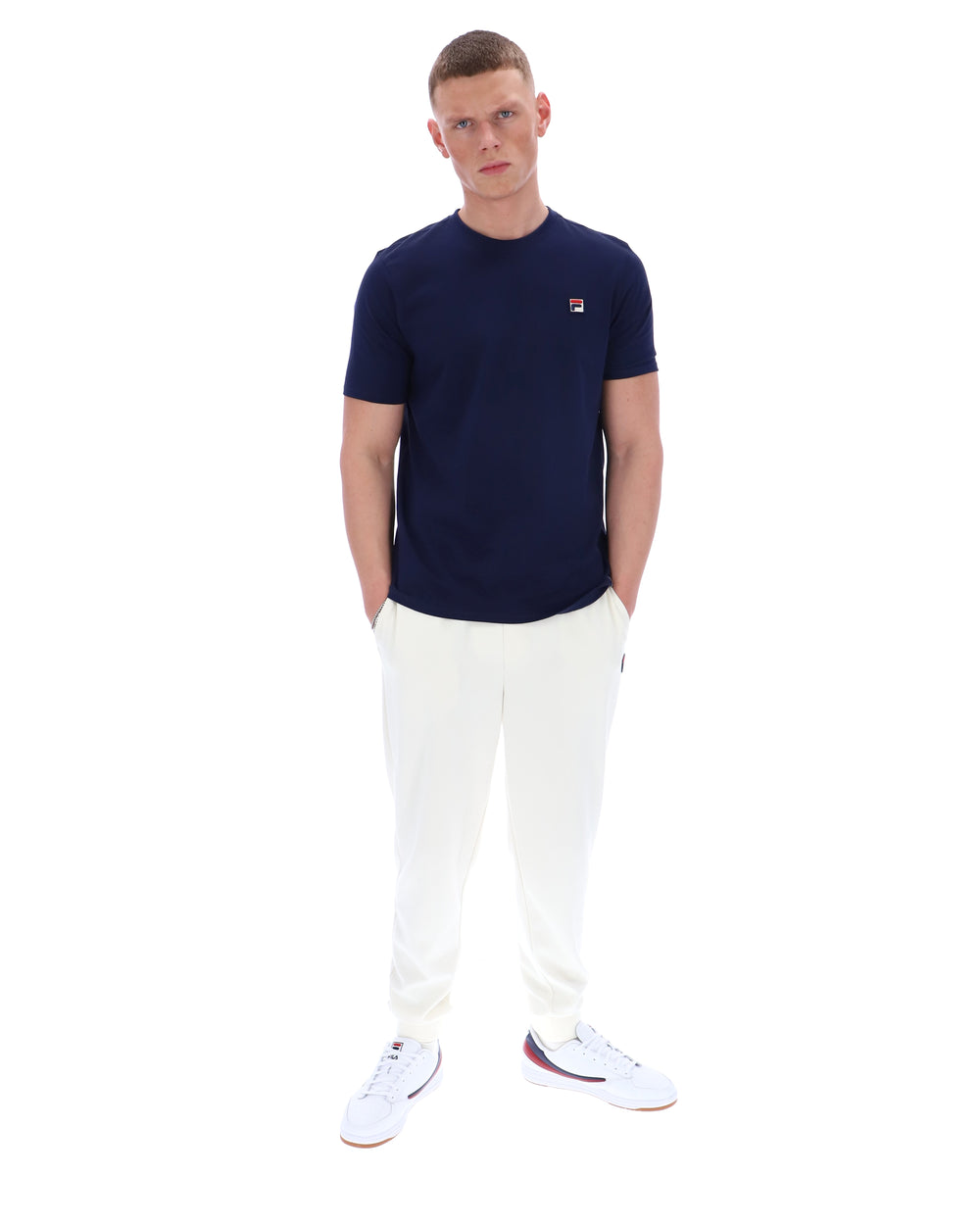 Man wearing a navy t-shirt and white pants on a white background