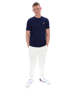 Man wearing a navy t-shirt and white pants on a white background
