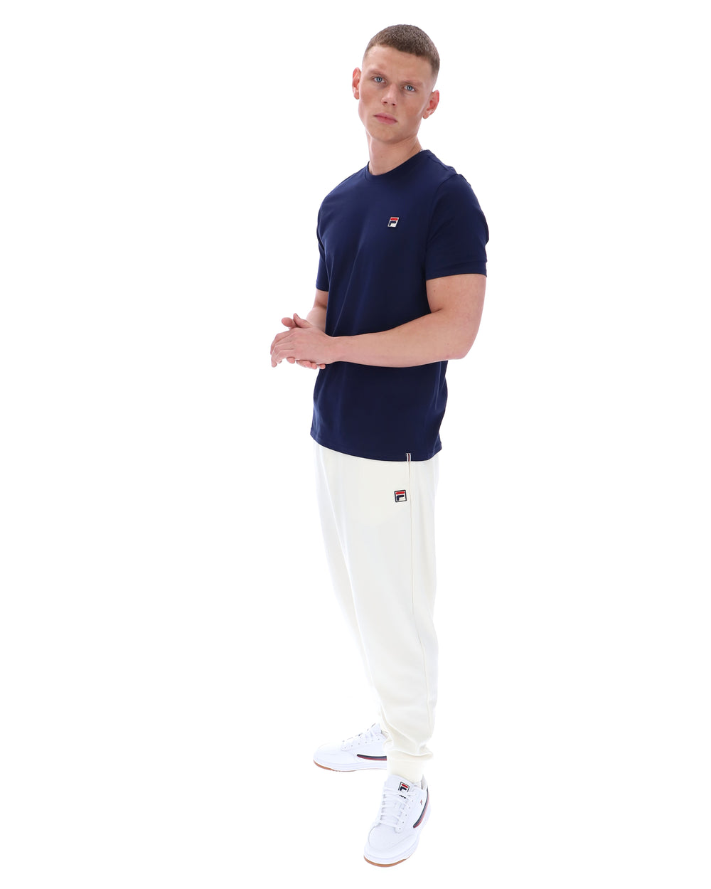 Man wearing a navy t-shirt and white pants on a white background