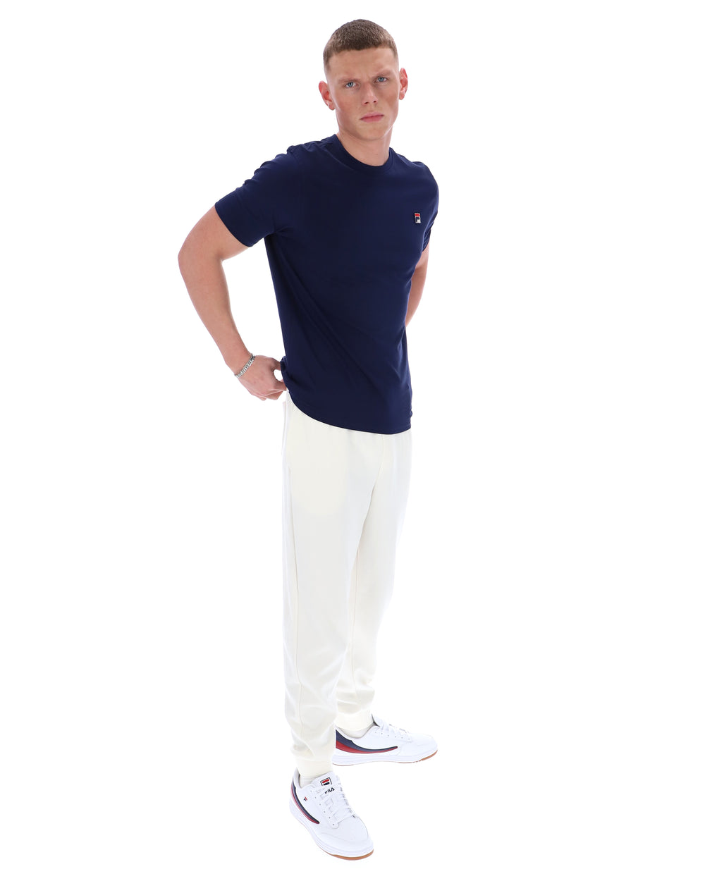 Man wearing a navy blue t-shirt and white pants on a white background
