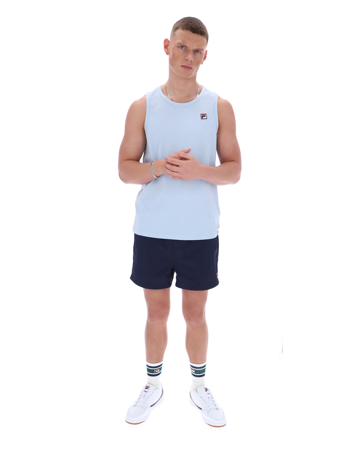 Man wearing a light blue sleeveless shirt and navy shorts on a white background