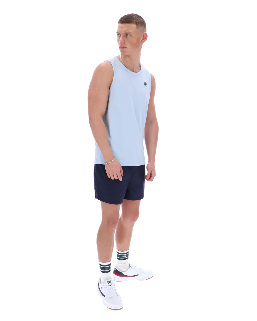 Man wearing a light blue sleeveless shirt and navy shorts on a white background