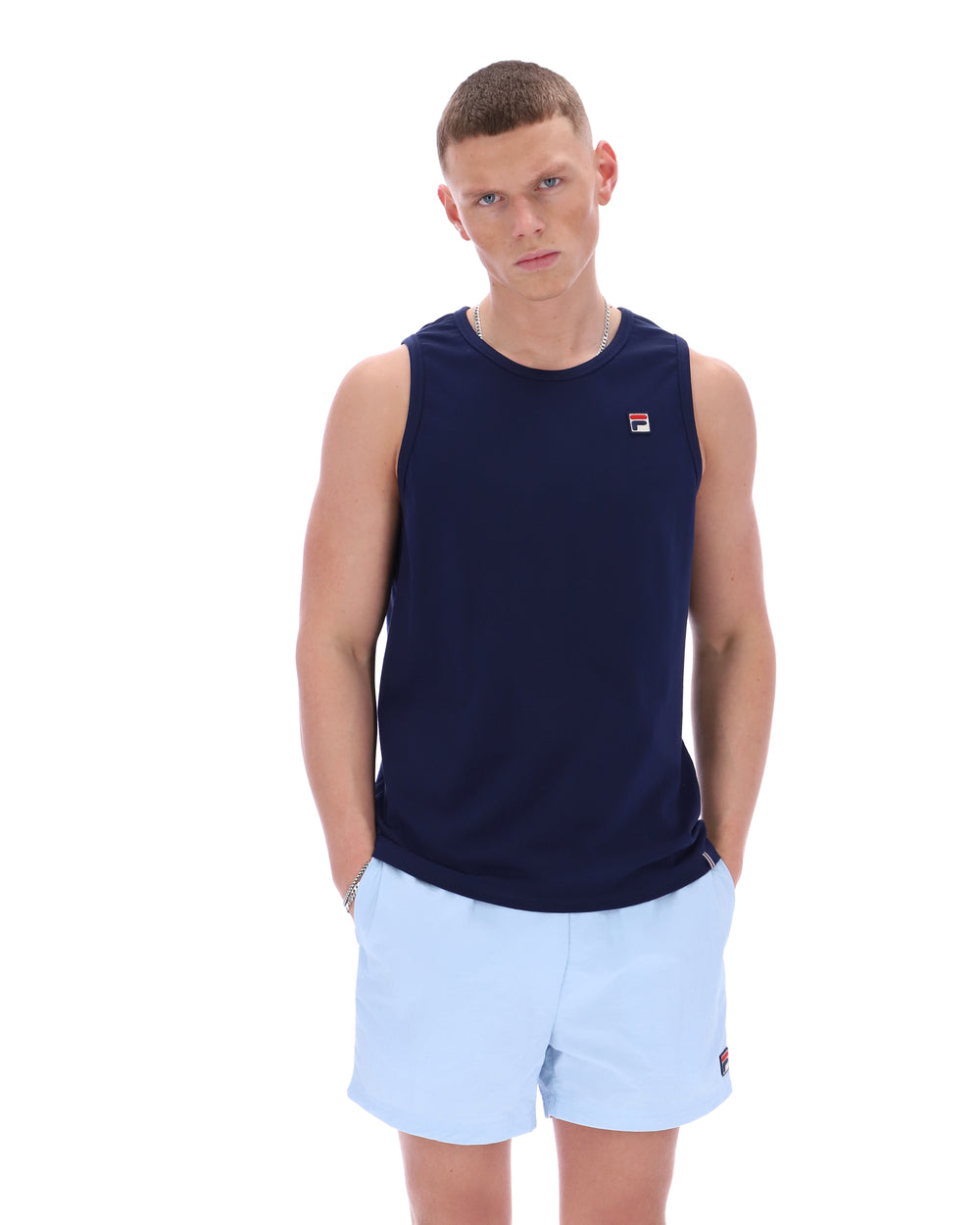 Man wearing a navy sleeveless shirt with a logo and light blue shorts on a white background