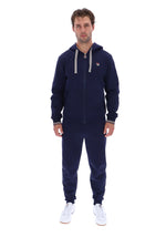 A man modeling a navy blue zip-up hoodie and matching sweatpants set with white drawstrings and white sneakers, photographed against a solid white background.