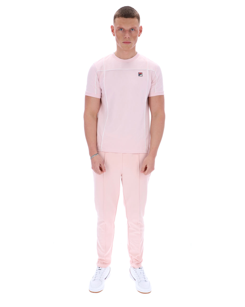 Man wearing a pink t-shirt with a FILA logo on the chest and matching trousers on a white background