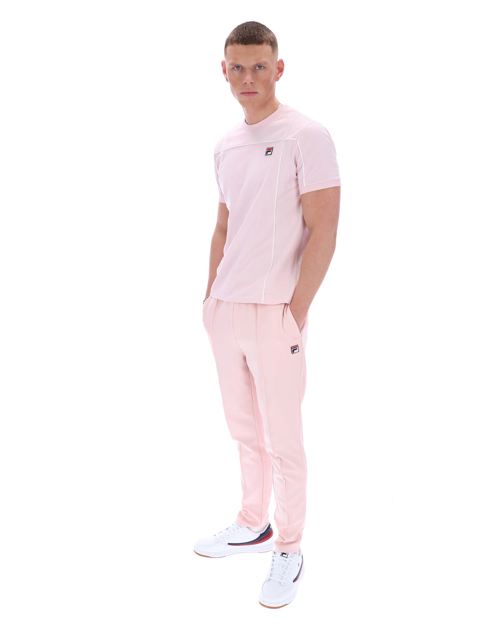 Man wearing a pink t-shirt with a FILA logo on the chest and matching trousers on a white background