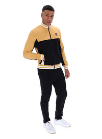 Man wearing a black and beige tracksuit with a FILA logo on the chest, paired with black FILA bottoms, against a white background