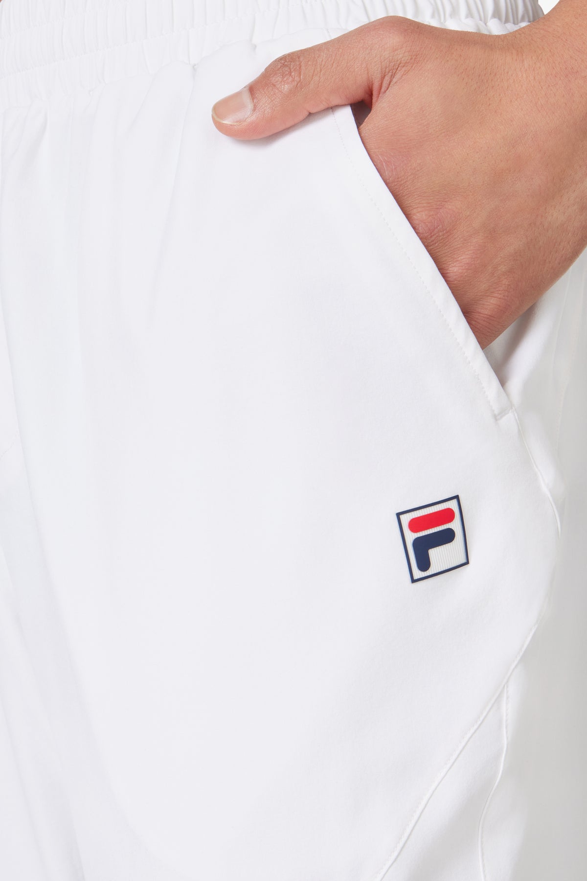 A person wearing white tennis court track pants with the FILA logo on the left leg by the pocket.