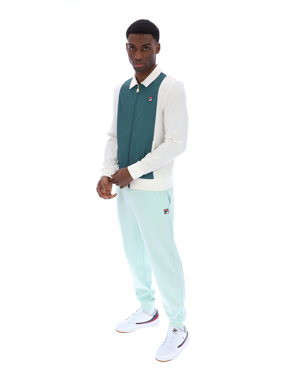 Man wearing a teal and white sweater with light blue pants on a white background