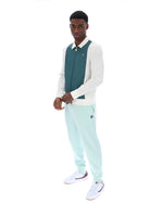 Man wearing a teal and white sweater with light blue pants on a white background