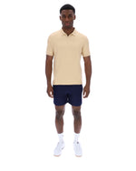 Man wearing a beige polo shirt and navy shorts on a white background