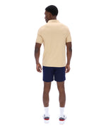 Man wearing a beige polo shirt and navy shorts on a white background