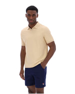 Man wearing a beige polo shirt and navy shorts on a white background