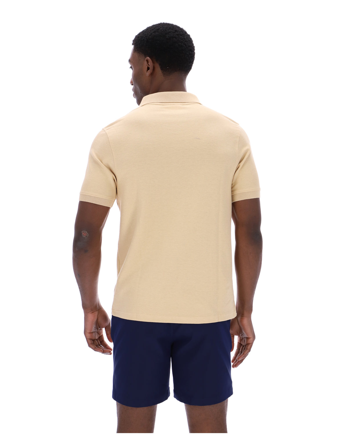 Man wearing a beige polo shirt and navy shorts on a white background