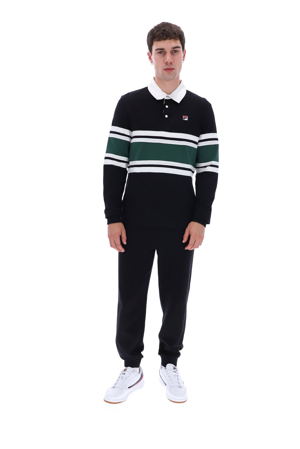 A young man modeling a black long-sleeve rugby shirt with green and white horizontal stripes, paired with black joggers and white sneakers, on a solid white background.