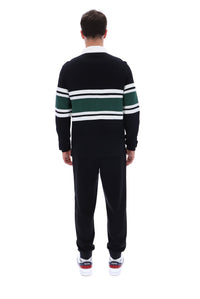 A man viewed from behind wearing a black knit sweater with green and white horizontal stripes across the shoulders and upper arms, paired with black sweatpants and white sneakers.