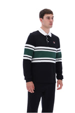 A man wearing a dark navy long-sleeve rugby-style sweater with horizontal white and green stripes across the chest and sleeves, paired with dark pants, photographed against a plain white studio background.