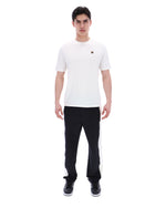 Man wearing a white t-shirt with a small FILA gold logo, paired with black pants, against a white background