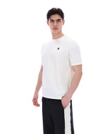 Man wearing a white t-shirt with a small FILA gold logo, paired with black pants, against a white background