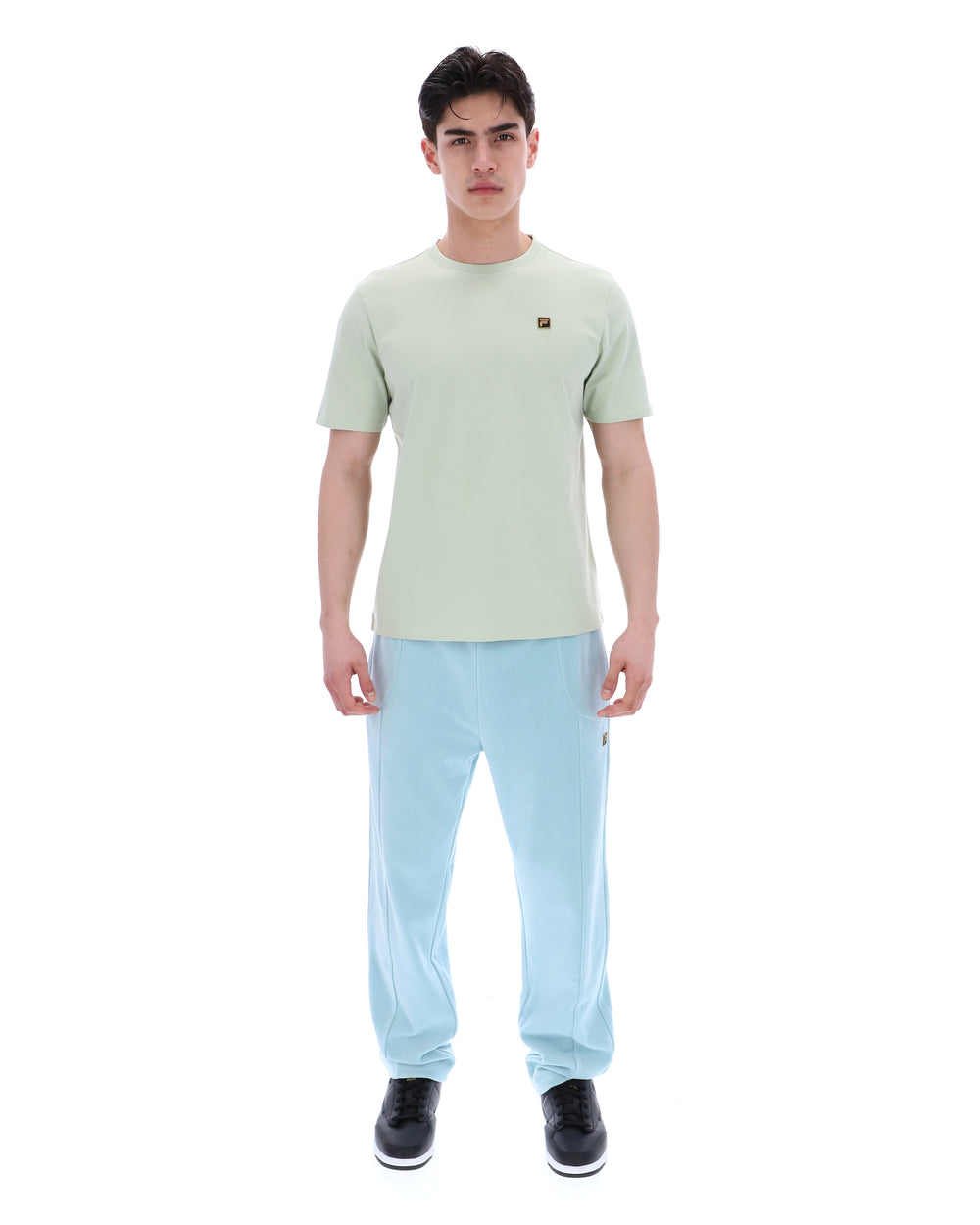 Person wearing a light green t-shirt with a FILA logo and light blue pants on a white background