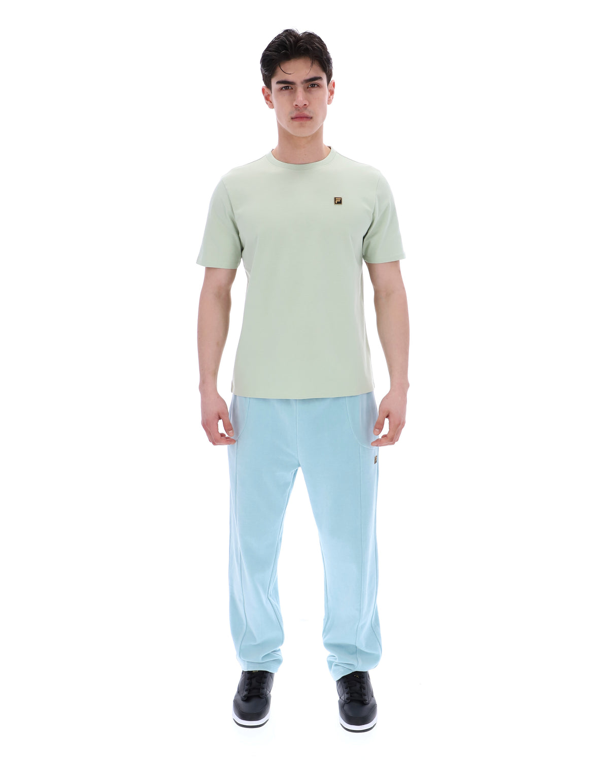 Person wearing a light green t-shirt with a FILA logo and light blue pants on a white background
