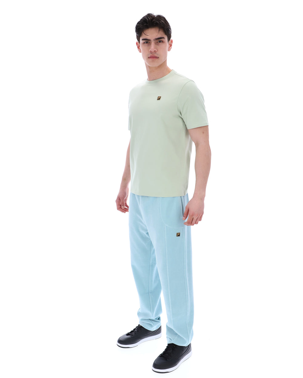 Person wearing a light green t-shirt with a FILA logo and light blue pants on a white background