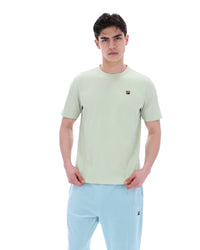 Person wearing a light green t-shirt with a FILA logo and light blue pants on a white background