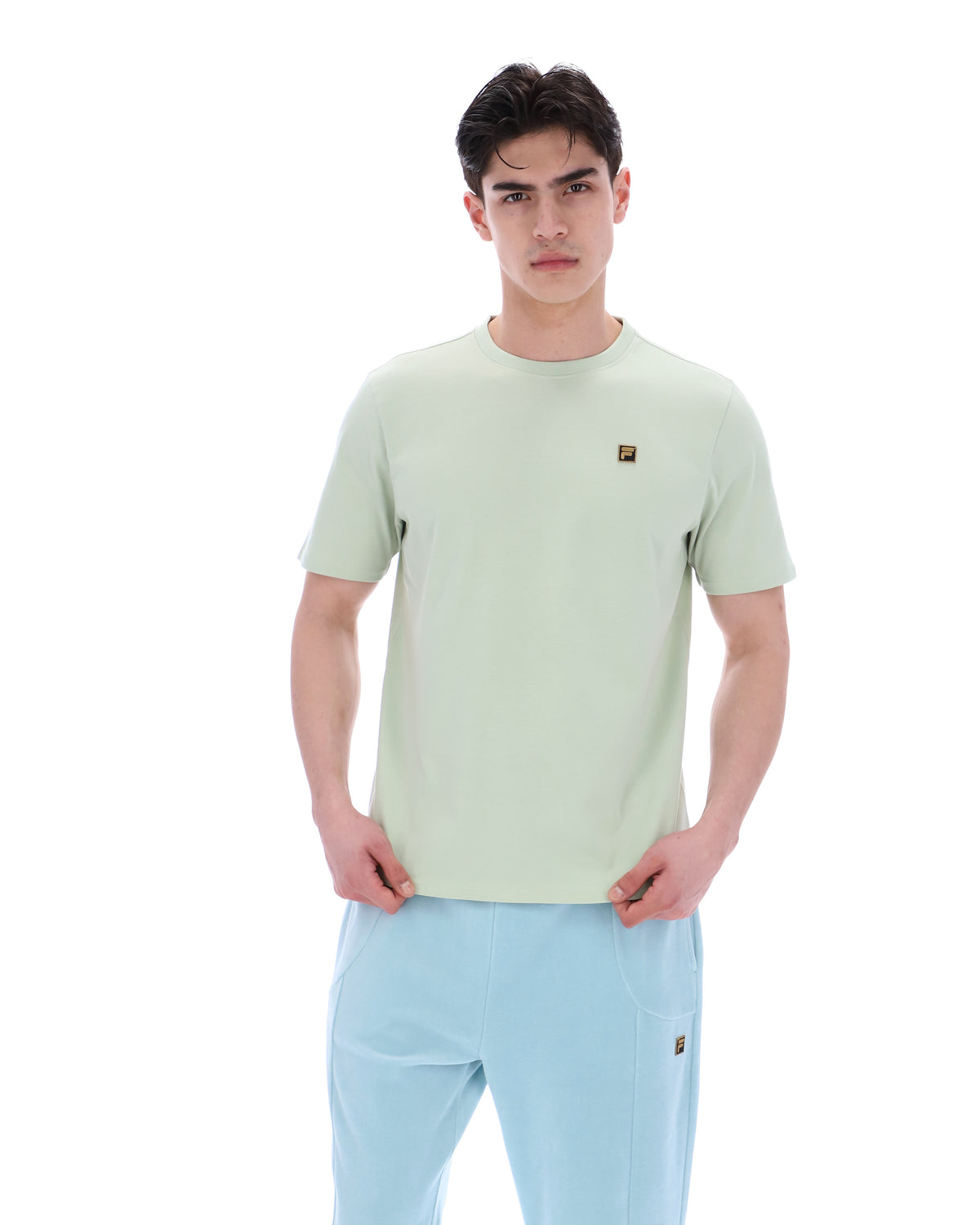 Person wearing a light green t-shirt with a FILA logo and light blue pants on a white background