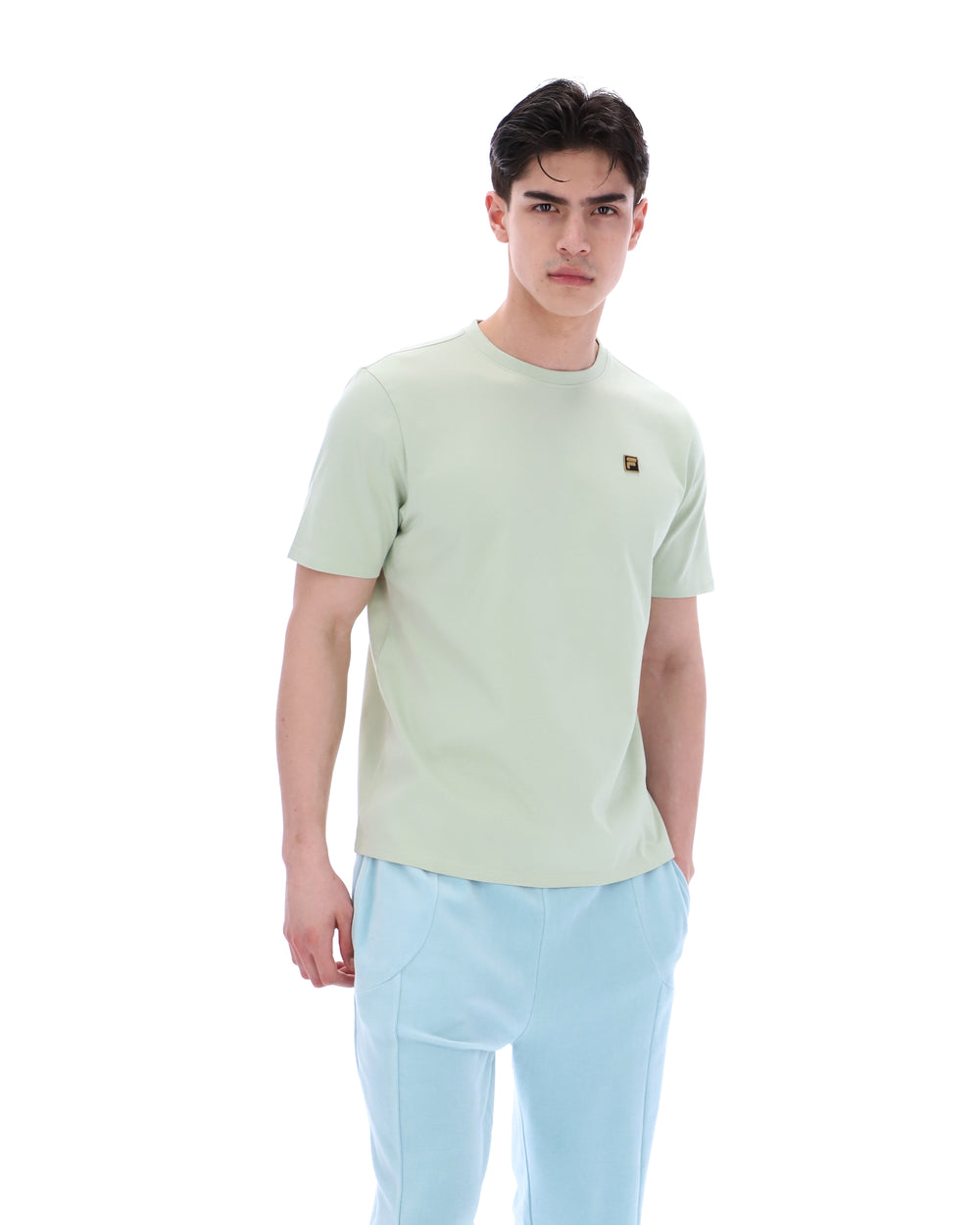 Person wearing a light green t-shirt with a FILA logo and light blue pants on a white background