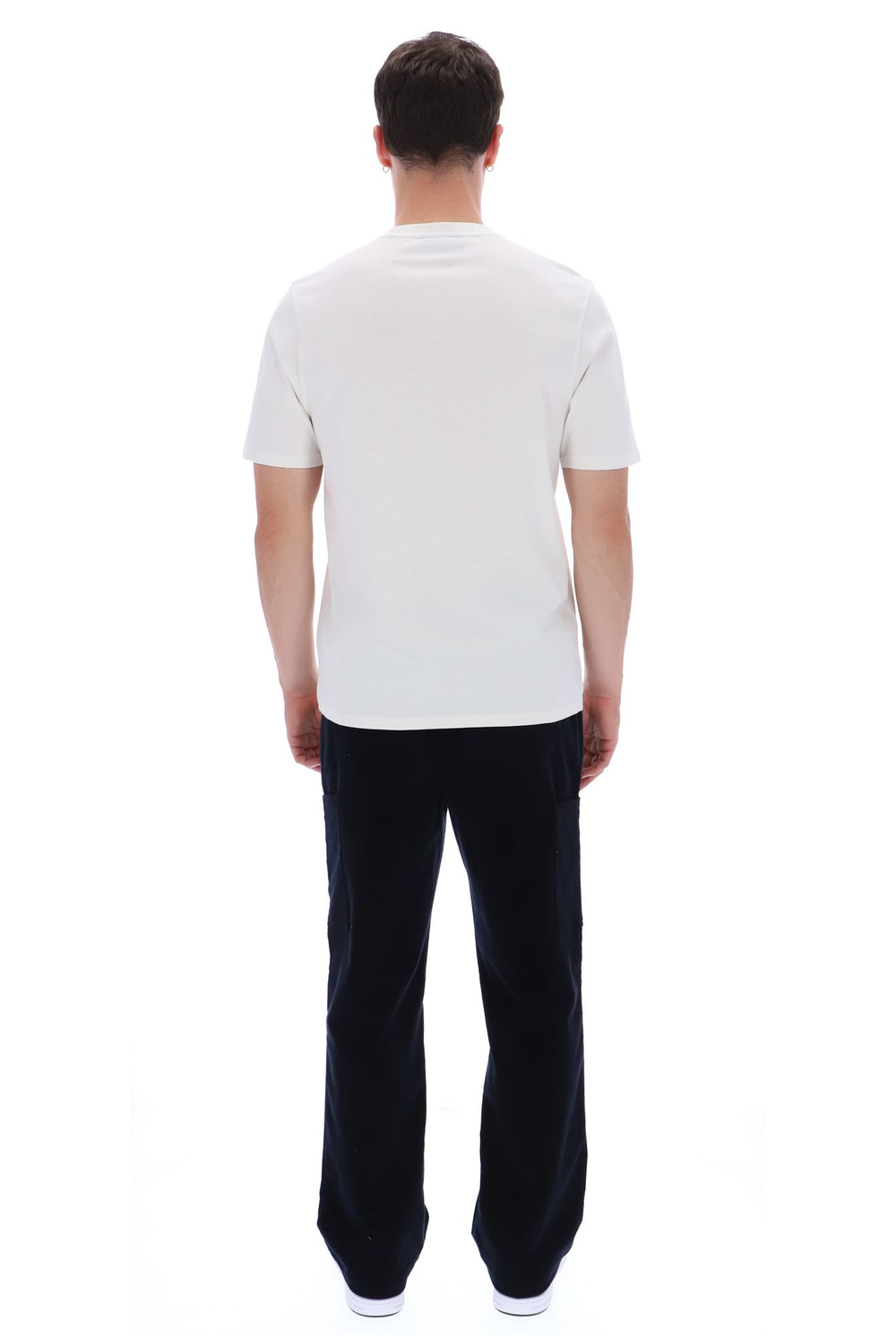 A man viewed from behind wearing a plain white short-sleeve t-shirt and dark navy pants, standing against a solid white background.