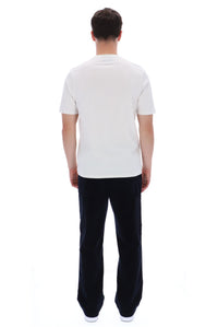 A man viewed from behind wearing a plain white short-sleeve t-shirt and dark navy pants, standing against a solid white background.