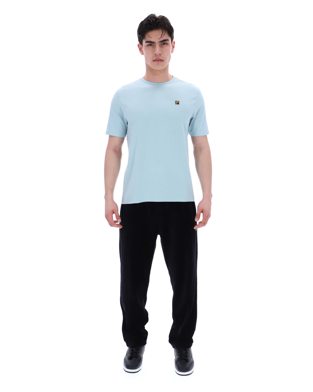 Man wearing a light blue t-shirt and black pants on a white background