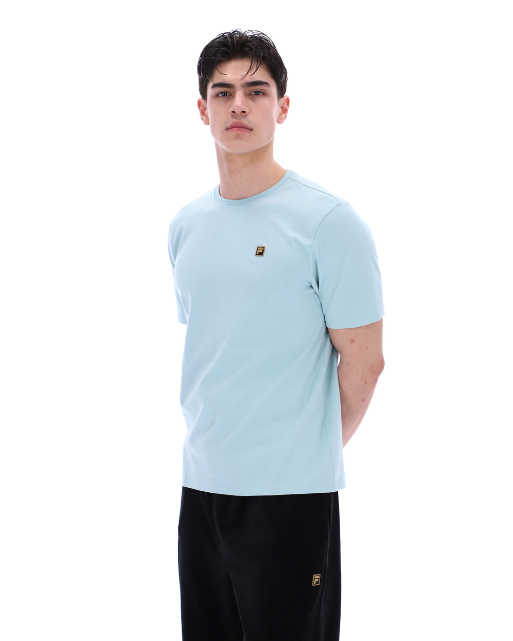 Person wearing a light blue t-shirt with a small logo on a white background