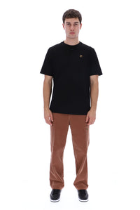 A man modeling a black short-sleeve crewneck t-shirt with a small embroidered logo on the left chest, paired with brown corduroy pants and black sneakers, against a plain white background.