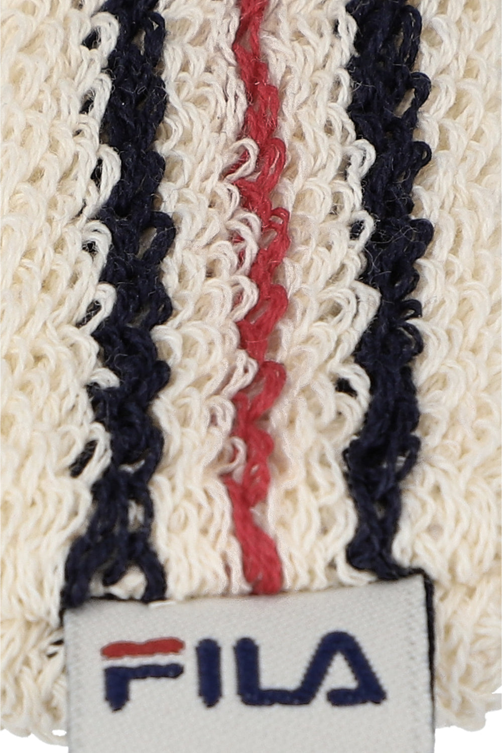 A close-up of a beige retro headband with a red and blue stripe pattern and the FILA logo embroidered on it.
