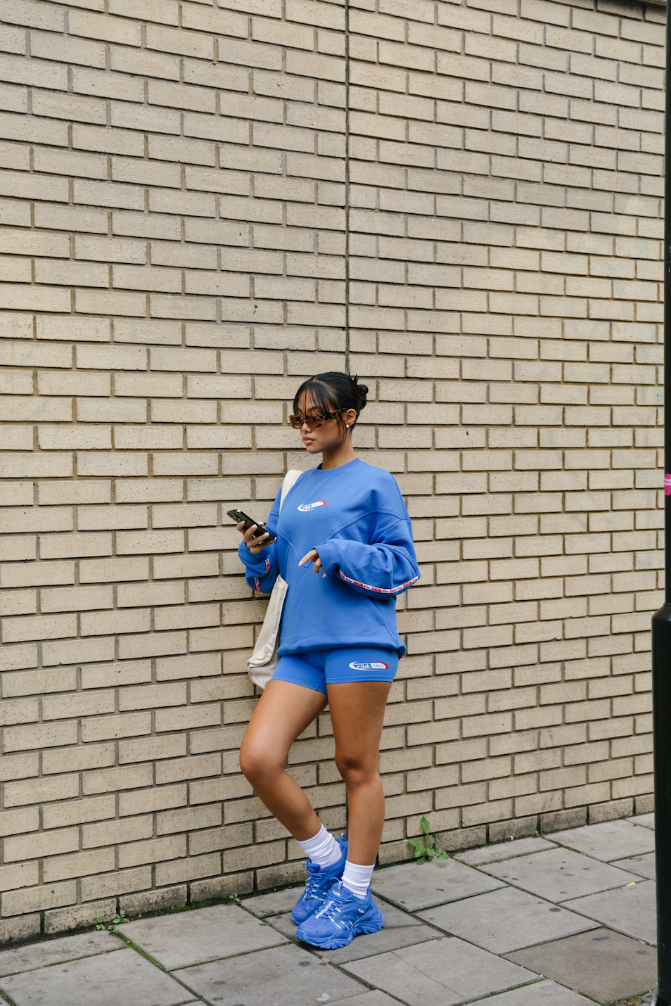 A person wearing blue high-waisted cycling shorts with the FILA x TALA brand logo on the front.