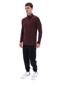 A man modeling a long-sleeve, high-neck burgundy turtleneck top paired with black sweatpants and white sneakers, set against a plain white background.
