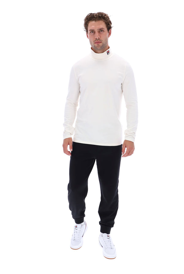 A man modeling a white long-sleeve mock neck sweater, black jogger pants, and white sneakers against a solid white background.