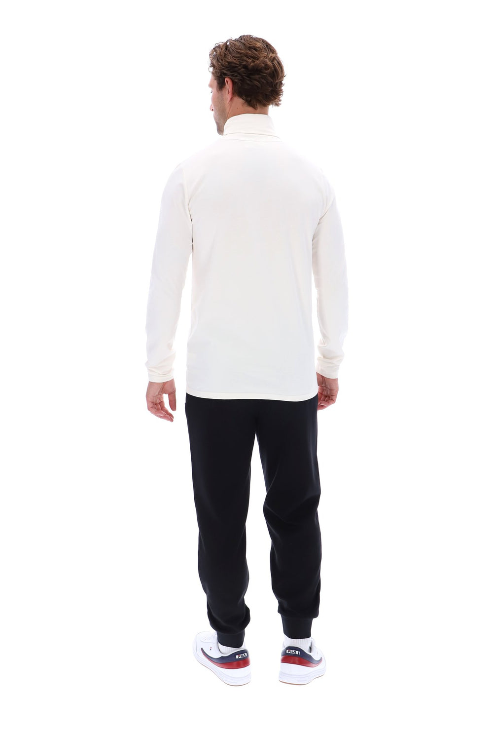 A man viewed from behind wearing a cream-colored long-sleeve mock neck top, black jogger pants, and white sneakers with red and blue accents, set against a plain white background.