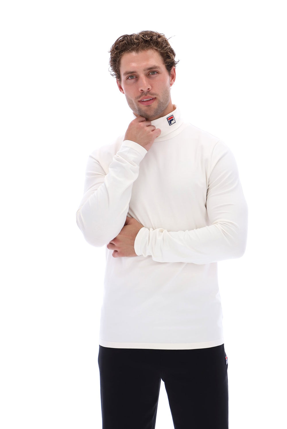 A man wearing a white long-sleeve mock neck shirt and black pants, posing against a solid white background.