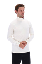 A man wearing a white long-sleeve mock neck turtleneck sweater and black pants, standing against a solid white background.