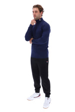 A man modeling a navy blue long-sleeve quarter-zip athletic top and black jogger pants with white sneakers, standing against a solid white background.