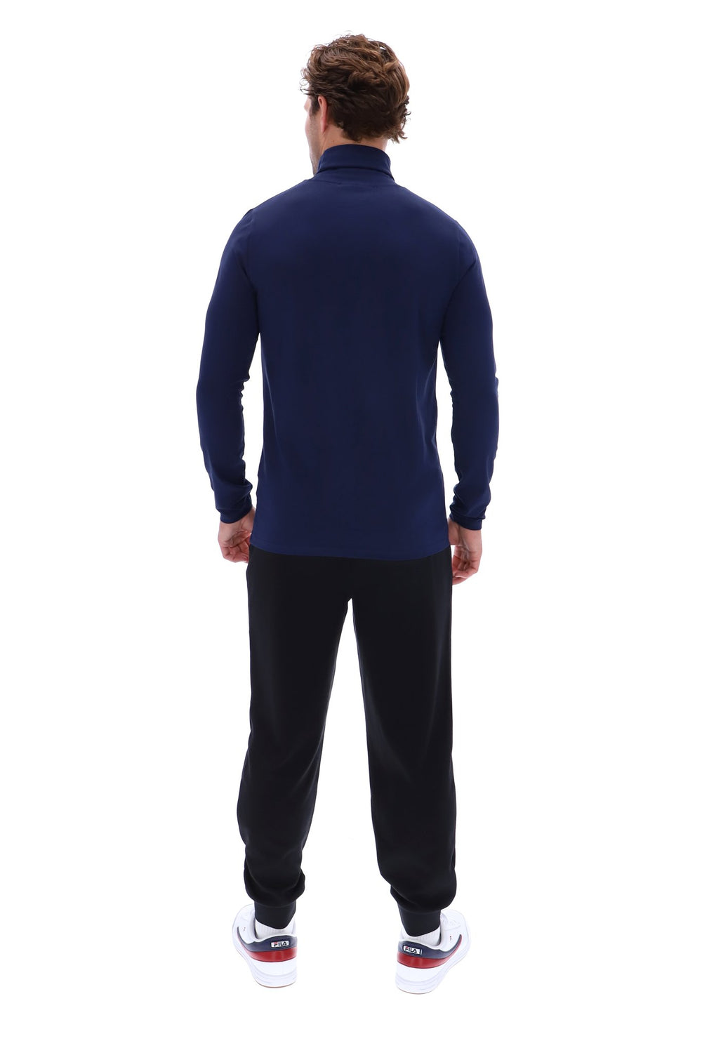 A man viewed from behind wearing a navy blue mock neck long-sleeve top, black sweatpants, and white sneakers with red and blue accents, set against a plain white background.